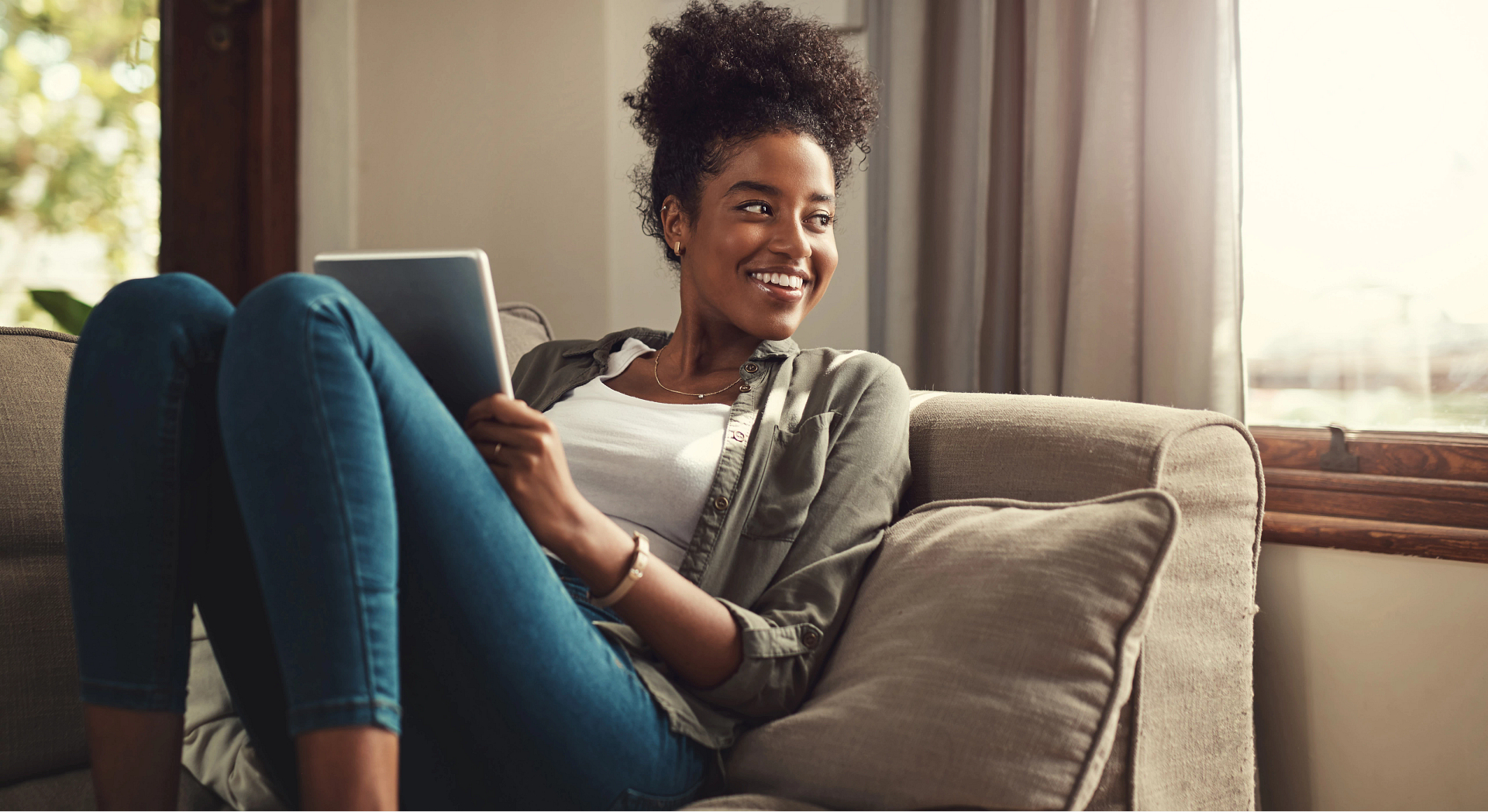 A smiling woman sitting on the couch holding a tablet device.