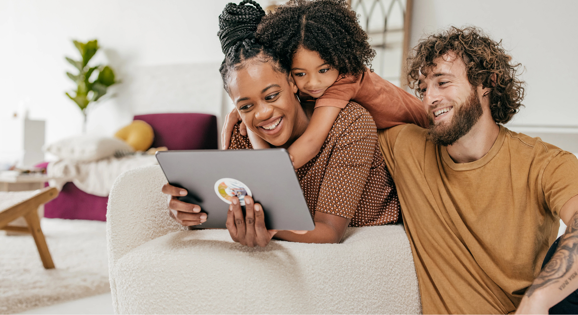 A family of three smiling while looking at a tablet.